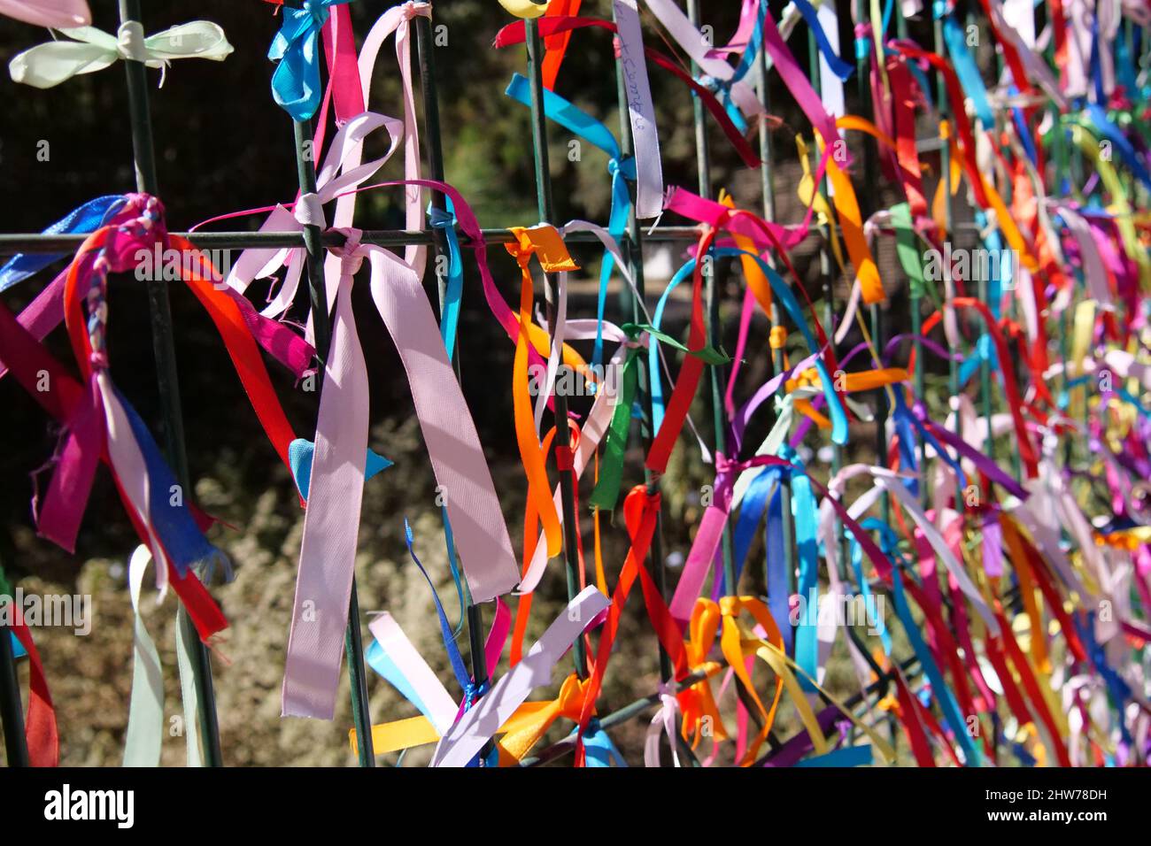 Colourful strings tied to a fence. Some of the strings have messages written on them. The background is intentionally out of focus or blurred. Stock Photo