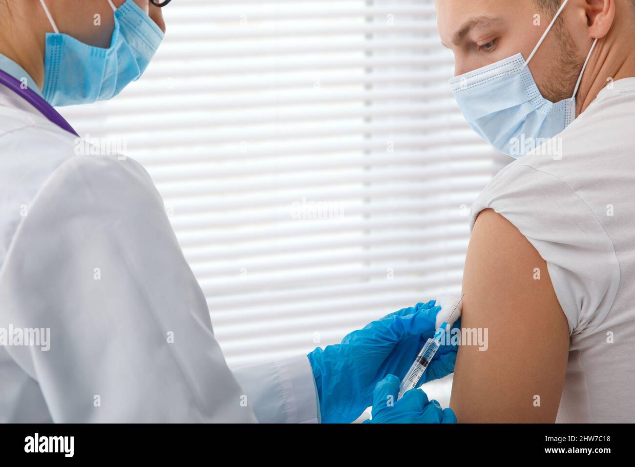 The doctor holds a syringe before giving an injection to a patient in a medical mask. Covid-19 or coronavirus vaccine. Vaccination of the population Stock Photo