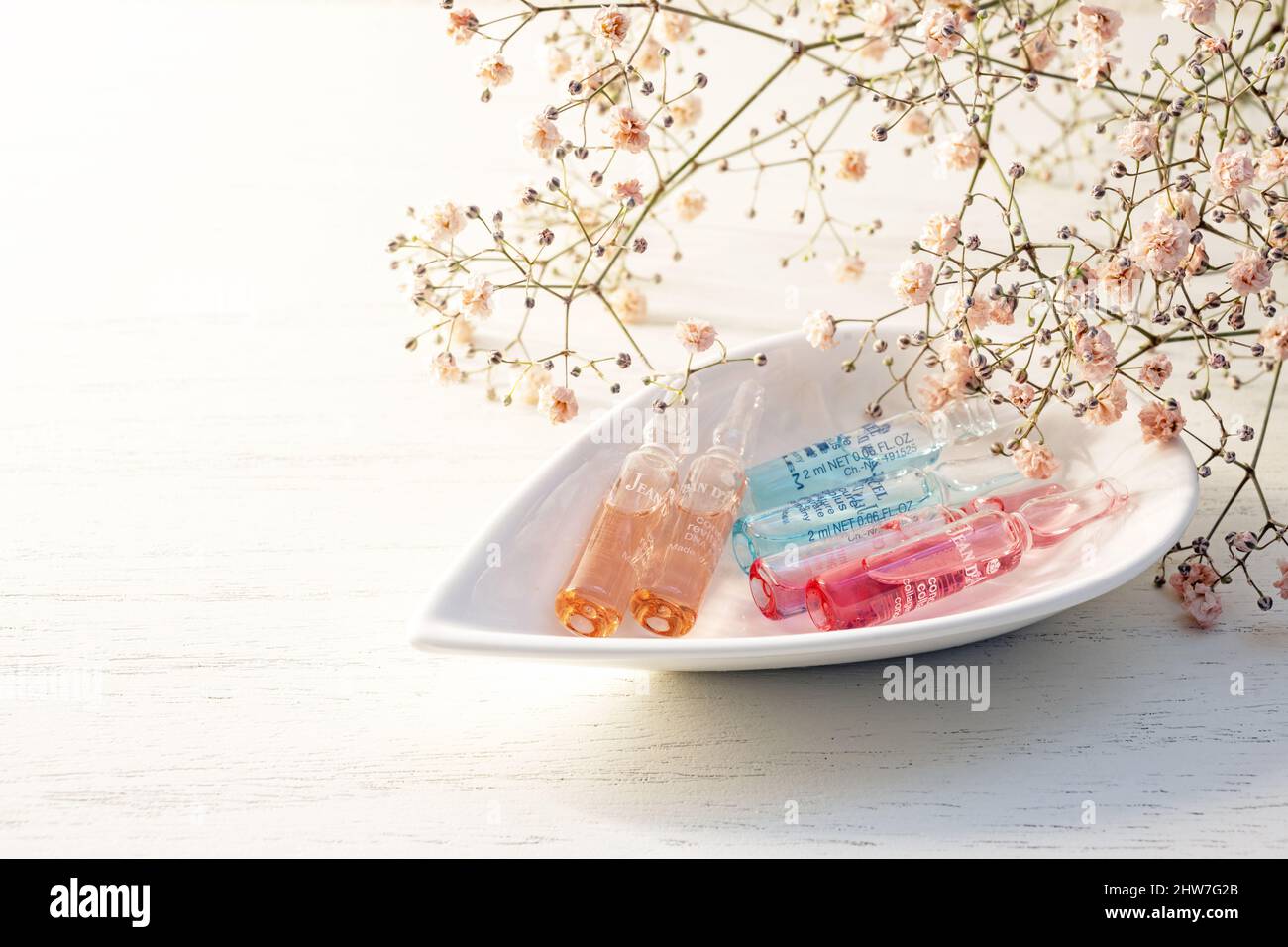 Lubeck, Germany, March 03, 2021: Ampoules from Jean d Arcel for luxurious cosmetic beauty treatment in a bowl, blush gypsophila flowers and bright bac Stock Photo