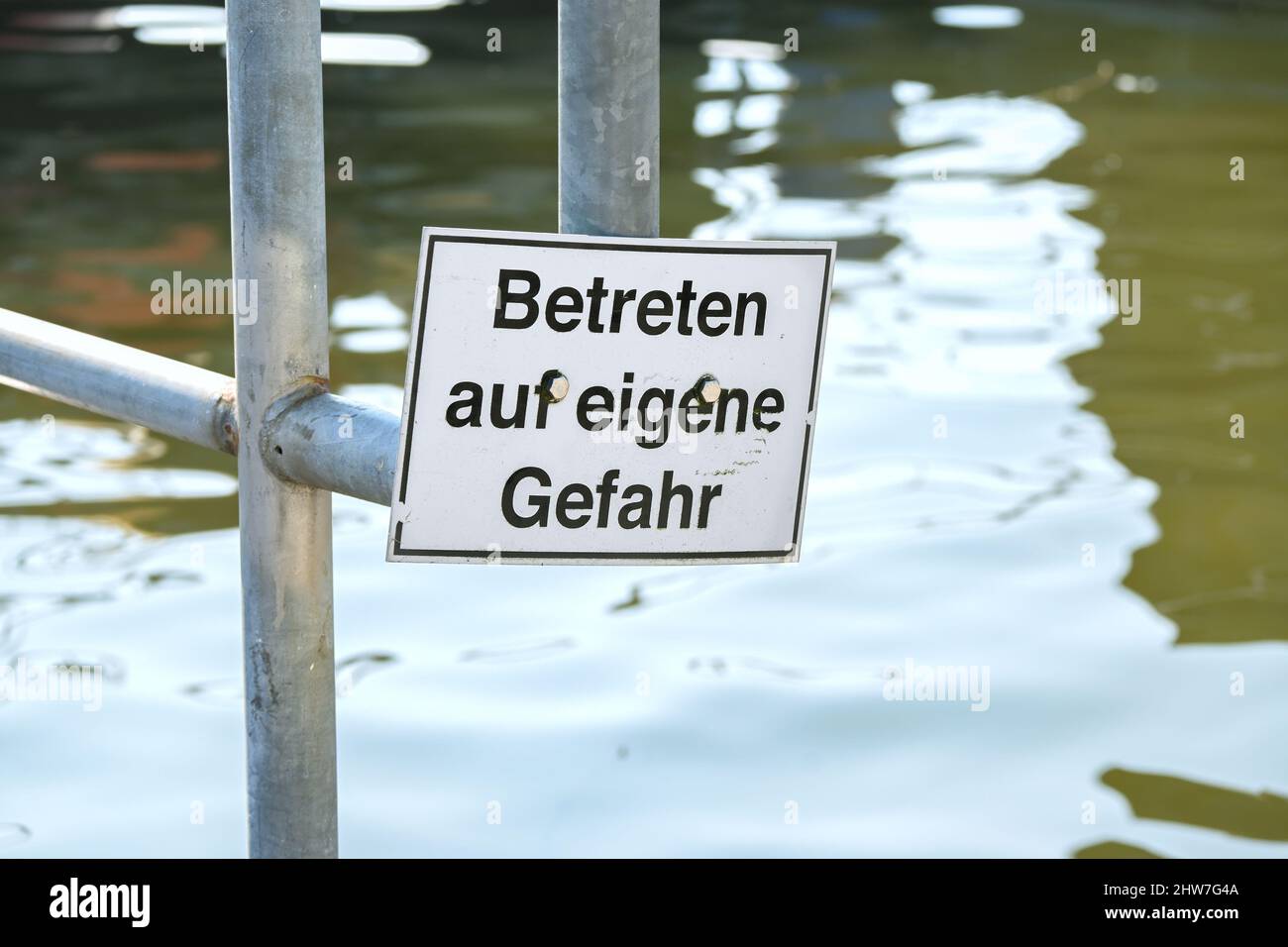 Warning sign at the quay edge in the port with German text, meaning Enter at your own risk, copy space in the water, selected focus, narrow depth of f Stock Photo