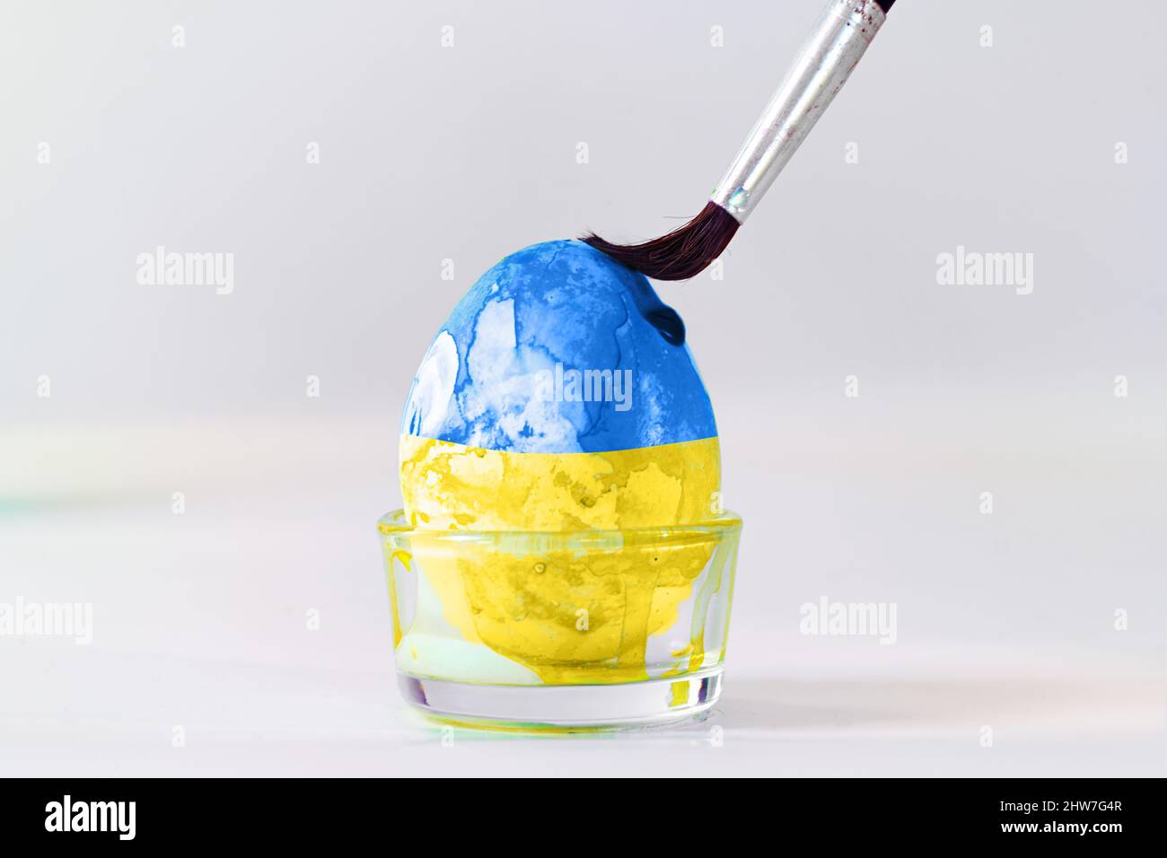 Brush is painting an Easter egg in blue and yellow, the colors of the ...