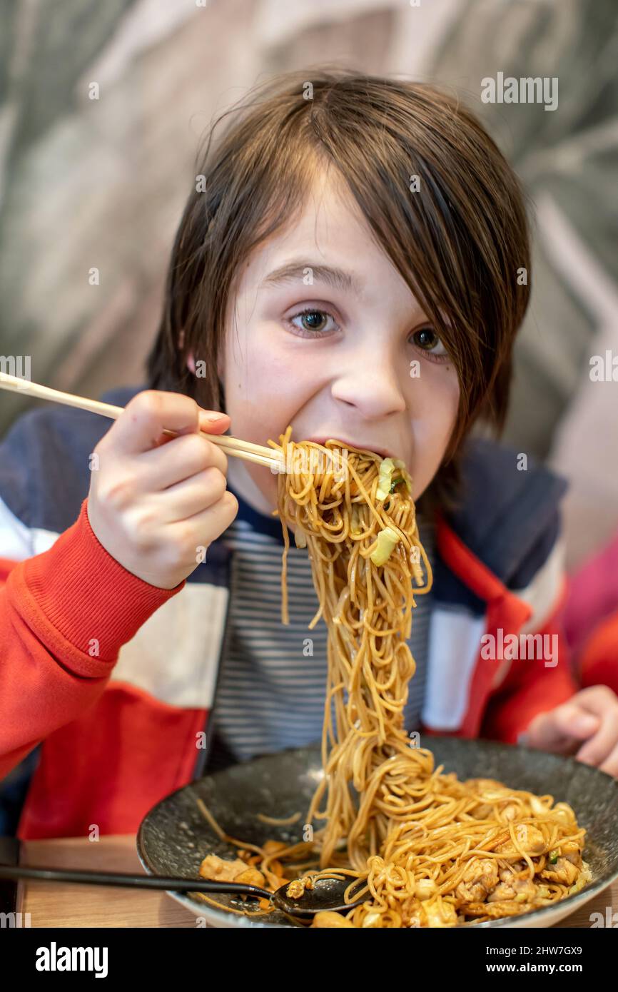 Child, eating japanese sushi and noodles with chopsticks in a restaurant, dinnertime Stock Photo