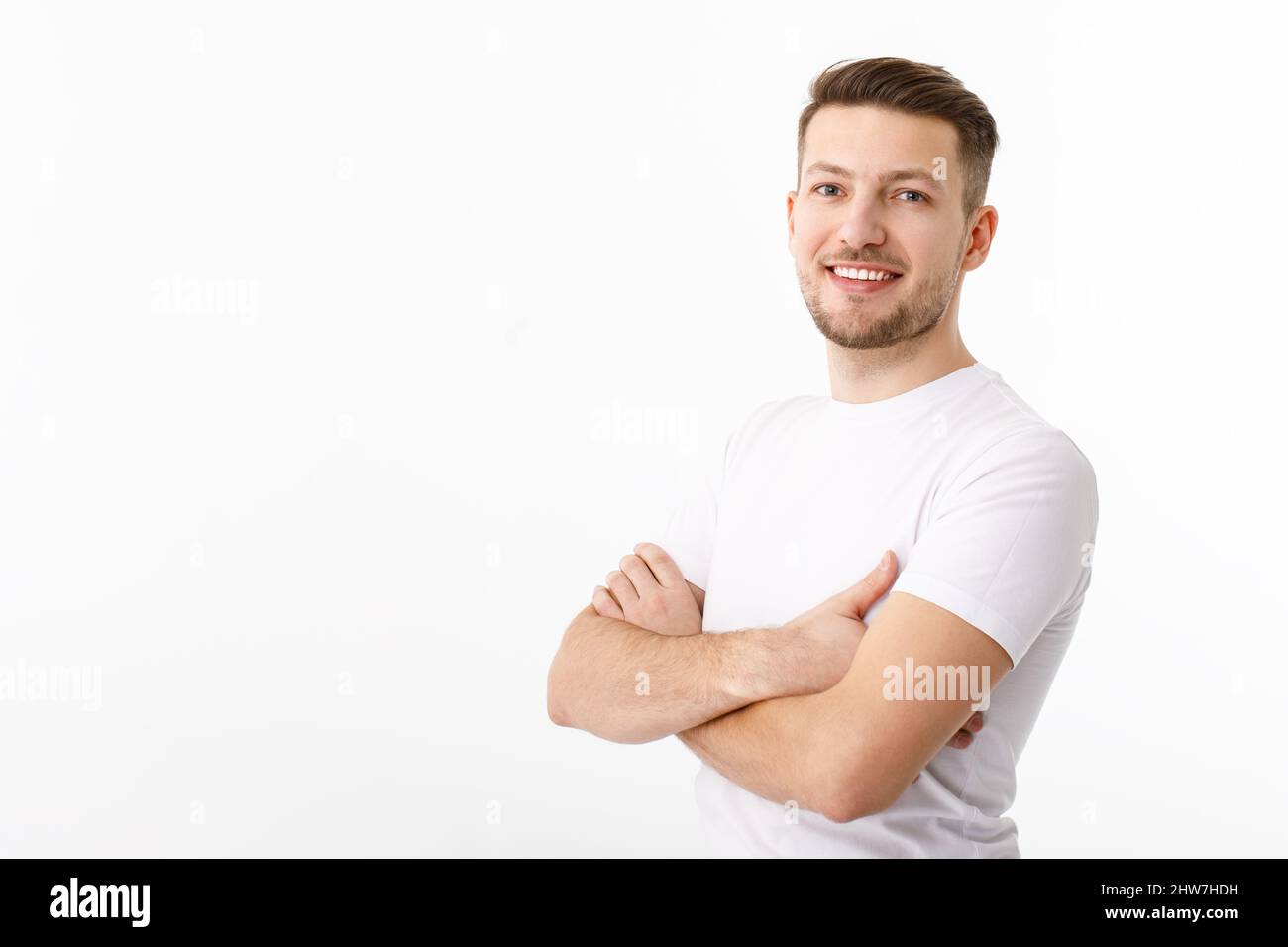 Portrait of a cheerful young man in a white T-shirt on a white background. The guy is standing looking at the camera and smiling. Stock Photo