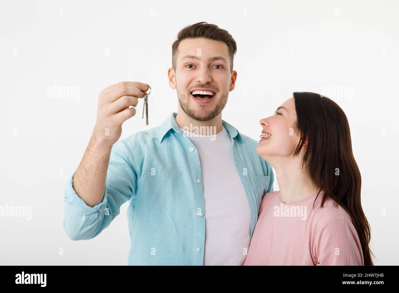 A cheerful young couple is hugging in the kitchen, holding the keys to a new house in their hands. Happy newlyweds moved into a new apartment, got a Stock Photo