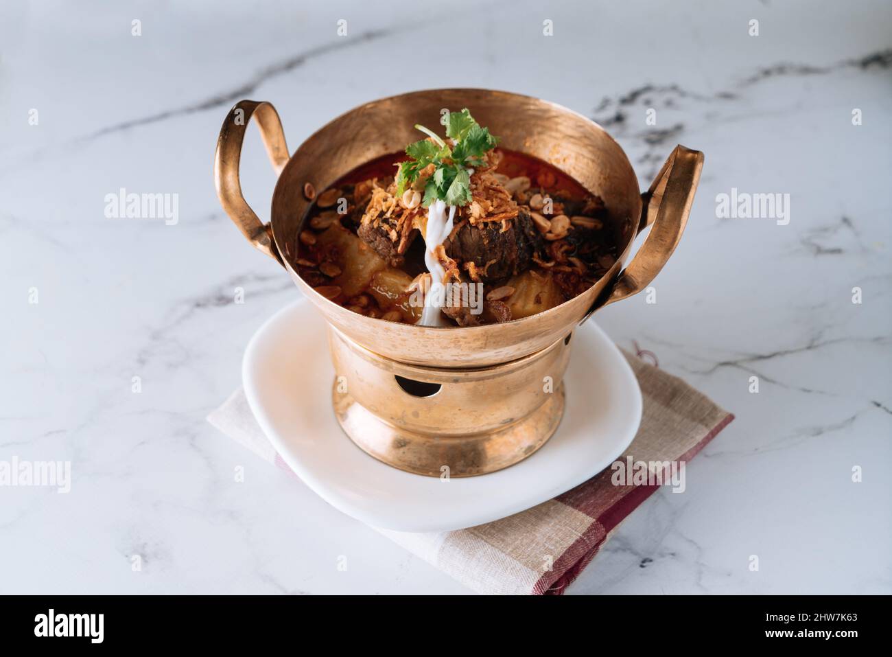 traditional Massaman Beef Curry in a copper stew dish isolated on mat top view on grey marble background Stock Photo