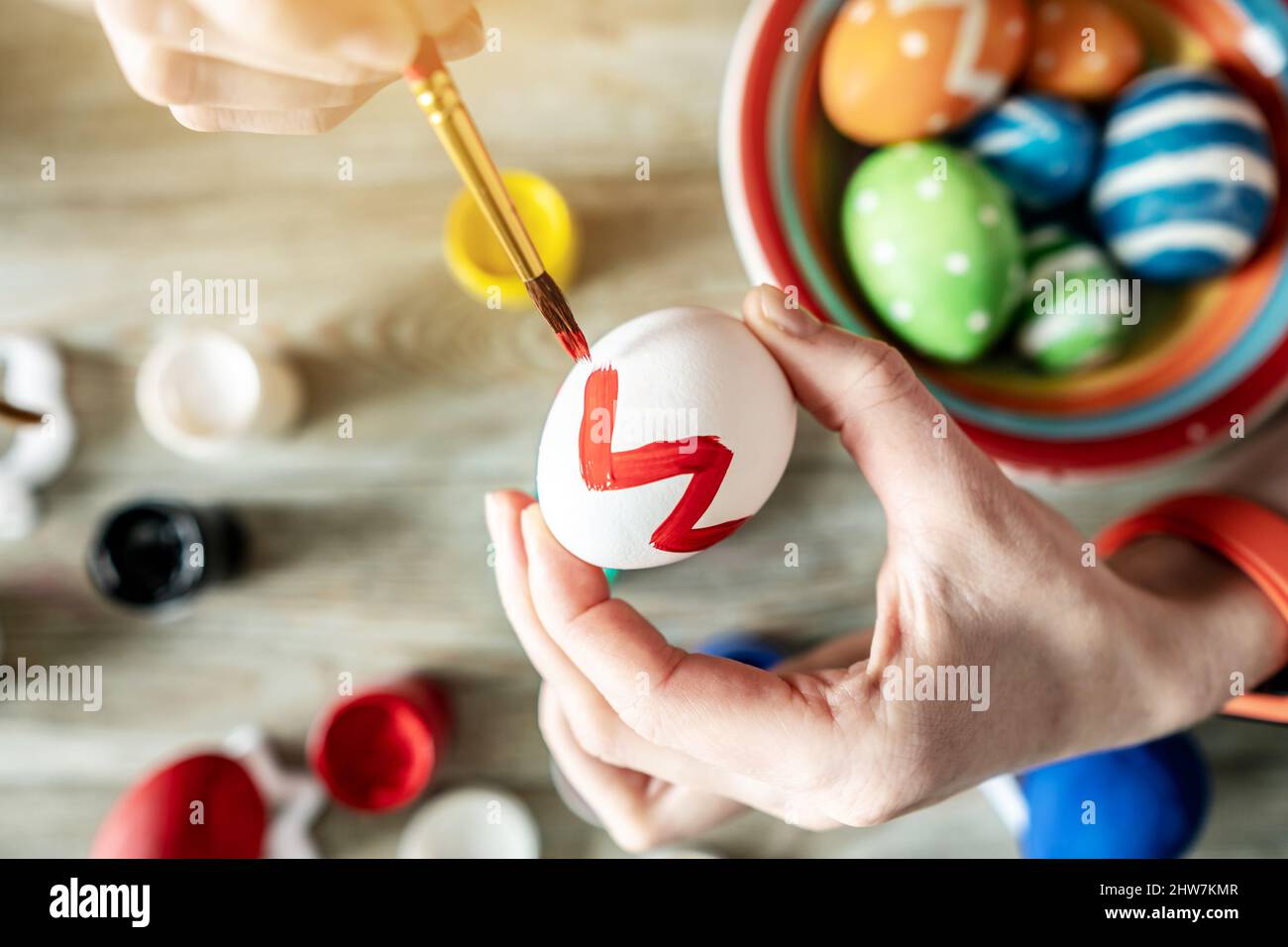 Woman's hand with a brush is drawing a colored pattern on an Easter egg. Creative preparation for bright Easter holiday Stock Photo