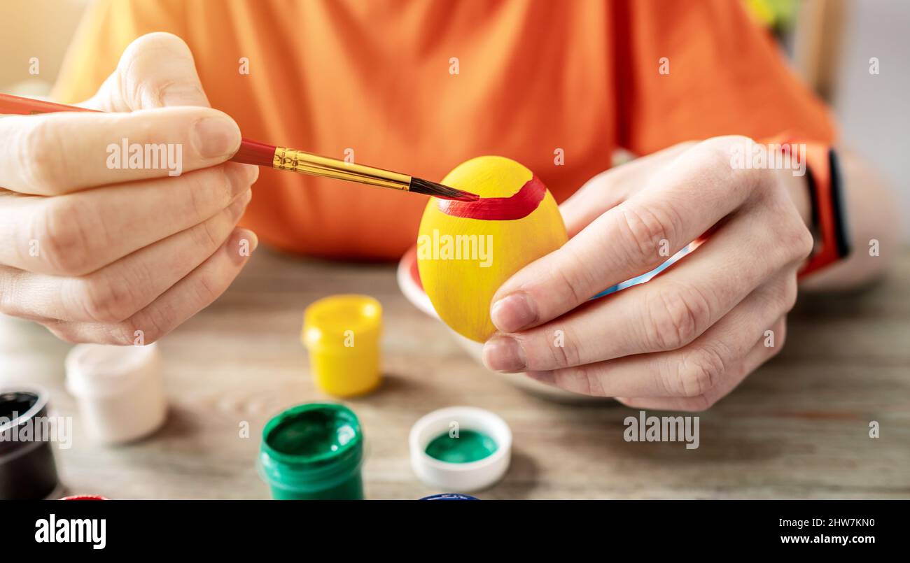 Woman's hand with a brush is drawing a colored pattern on an Easter egg. Creative preparation for bright Easter holiday Stock Photo