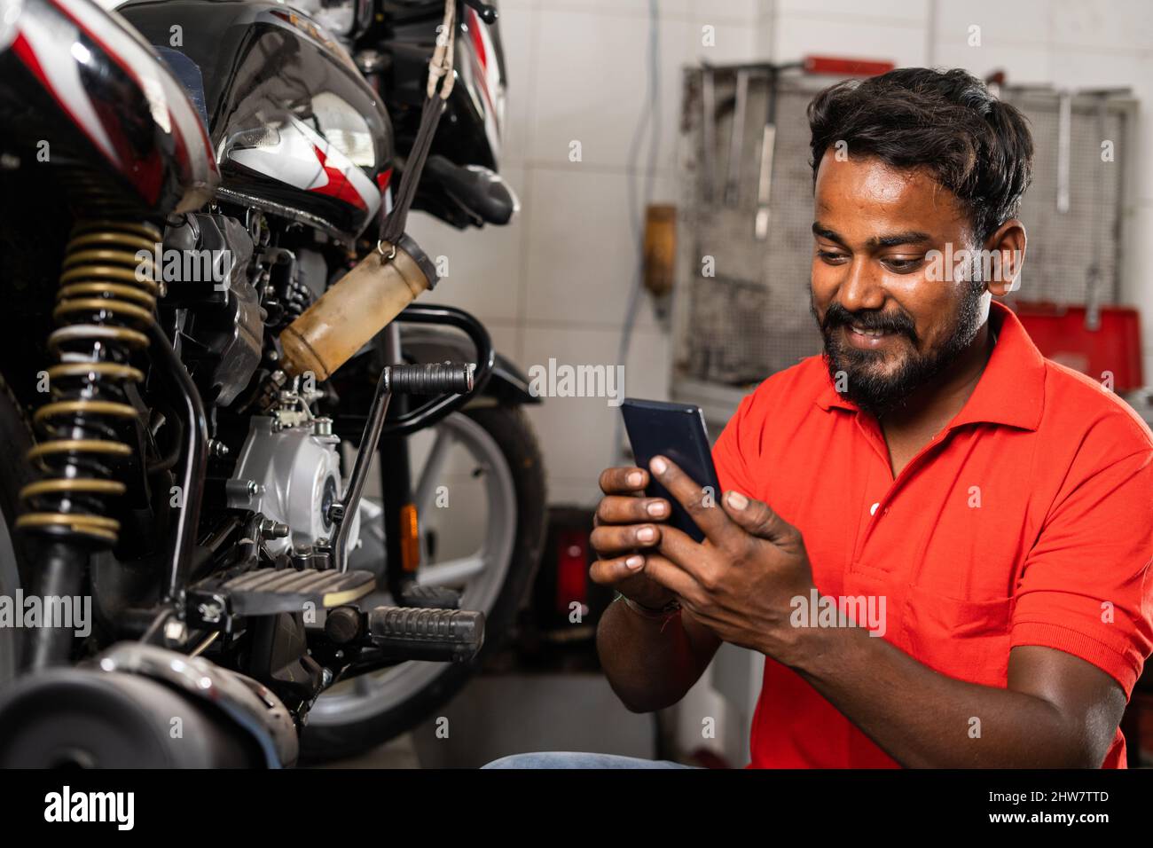 Young smiling mechanic using mobile phone in front of motors in showroom - concept of relaxation, taking break time and reading messages Stock Photo