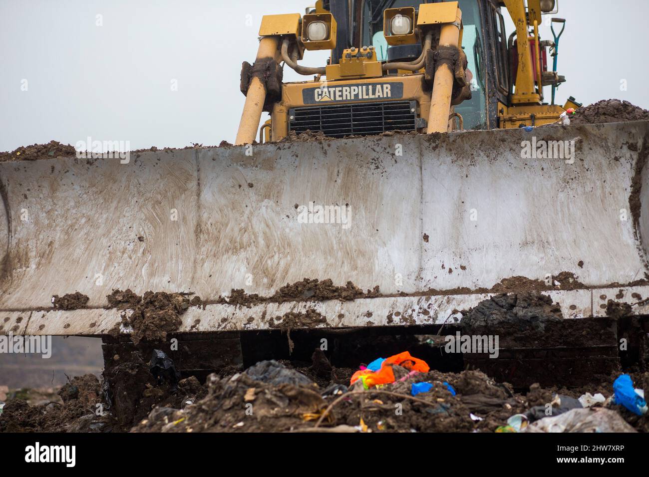 A Caterpillar bulldozer blade and tracks compact household waste on a UK waste disposal site. Stock Photo
