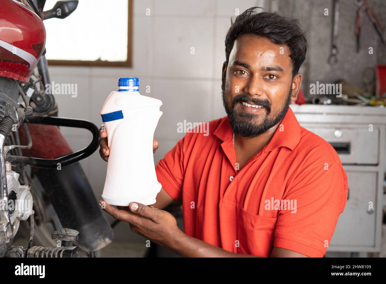smiling mechanic showing engine oil by looking at camera at garage - concept of product advertisment, promotion and recommending Stock Photo