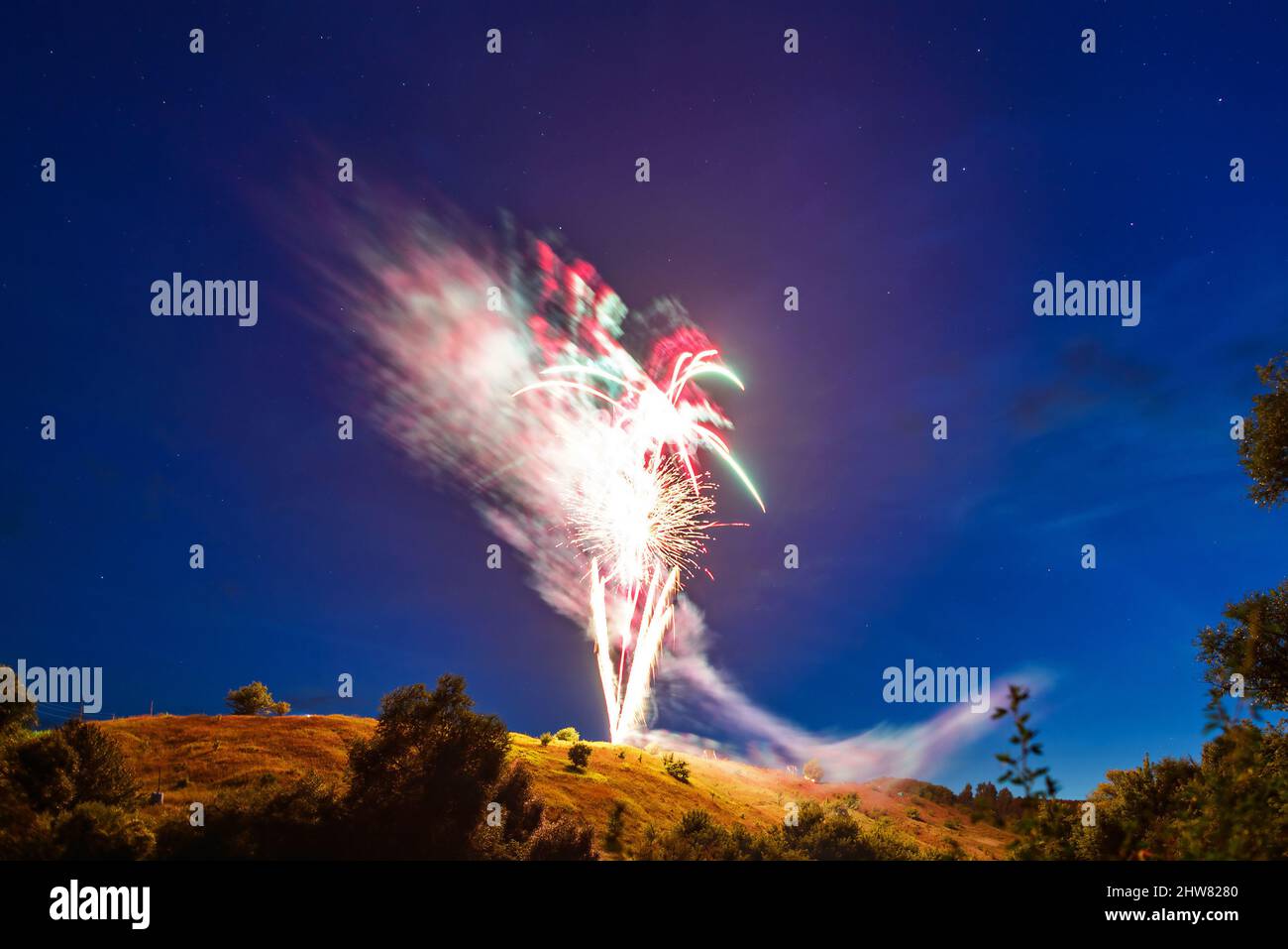 Bright fireworks over a hill in a natural landscape at night against a starry sky, a rural holiday landscape Stock Photo