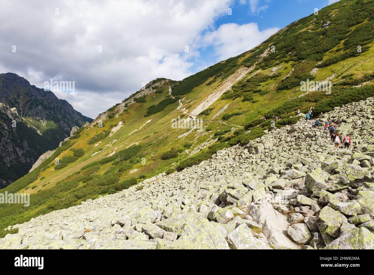 Tourists hiking in Tatra Mountains under blue cloudy sky Stock Photo