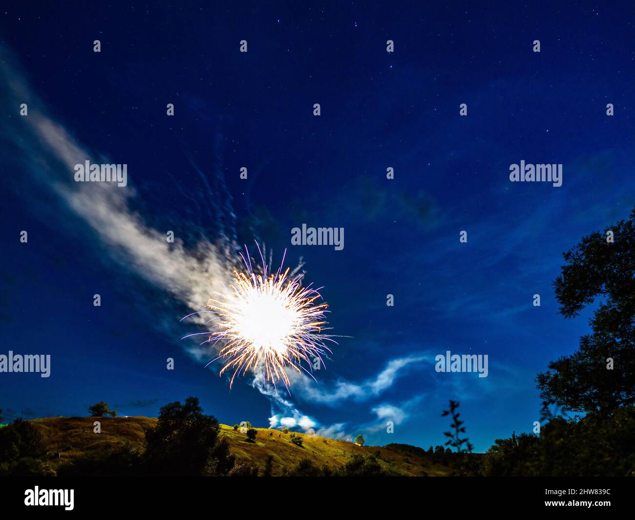 Bright fireworks over a hill in a natural landscape at night against a starry sky, a rural holiday landscape Stock Photo