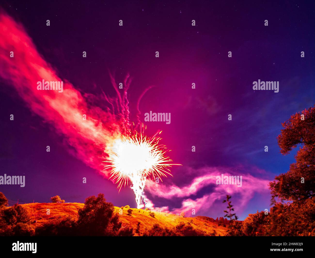 Bright red fireworks over a hill in a natural landscape at night against a starry sky, a rural holiday landscape Stock Photo