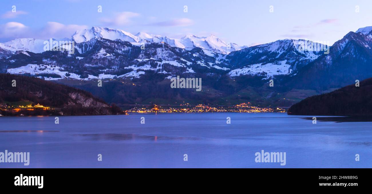 Switzerland, Alps peaks in the snow. Lake Lucerne. Evening lights of a small town Beckenried. Stock Photo