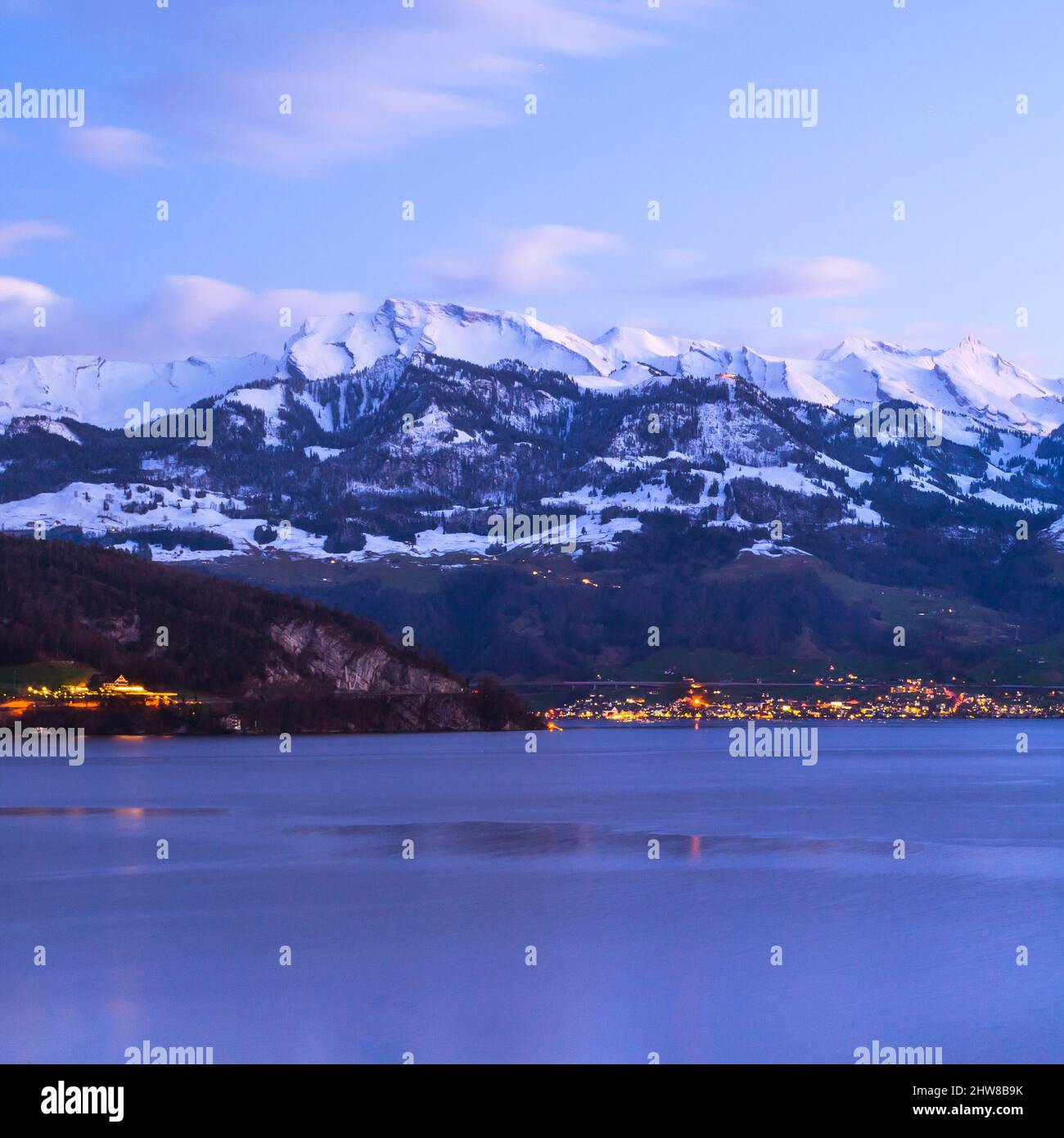 Switzerland, Alps peaks in the snow. Lake Lucerne. Evening lights of a small town Beckenried. Stock Photo