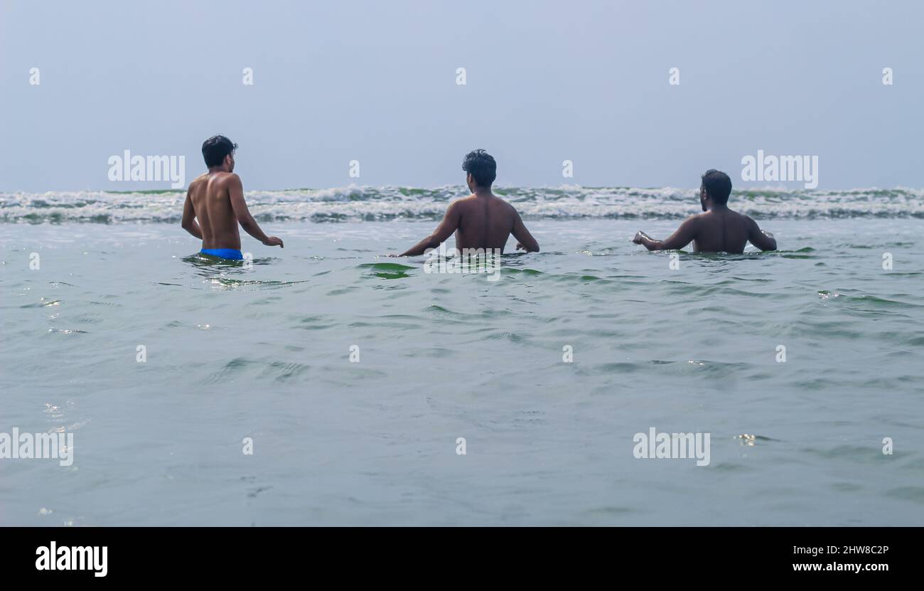 Happy friends are having fun and runs at sunrise beach to sun light and waves. Group of young boys playing together in the ocean waves. Stock Photo