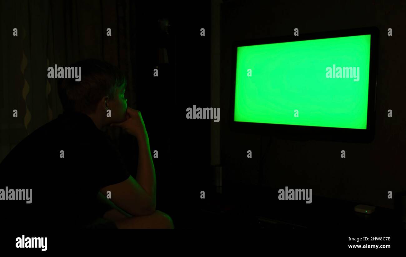 Side view of a young man watching TV with chromakey while sitting on a