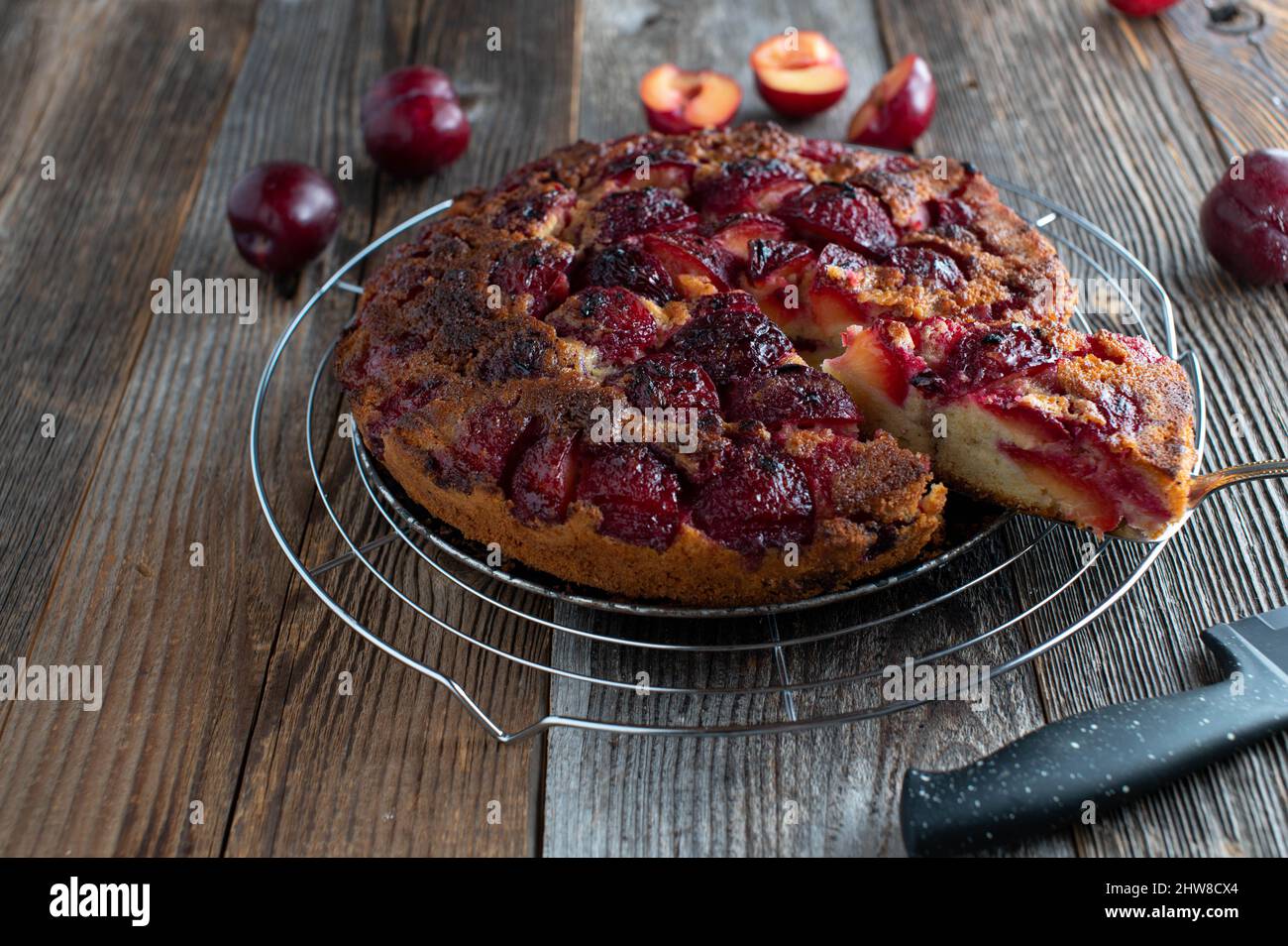 Plum cake baked upside down and served with cake server on a cooling rack isolated on dark wooden table Stock Photo