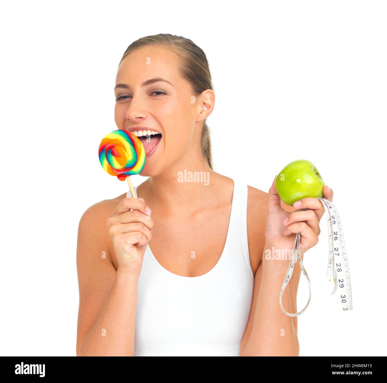 Portrait of a sporty young woman licking a lollipop while holding an apple. Stock Photo