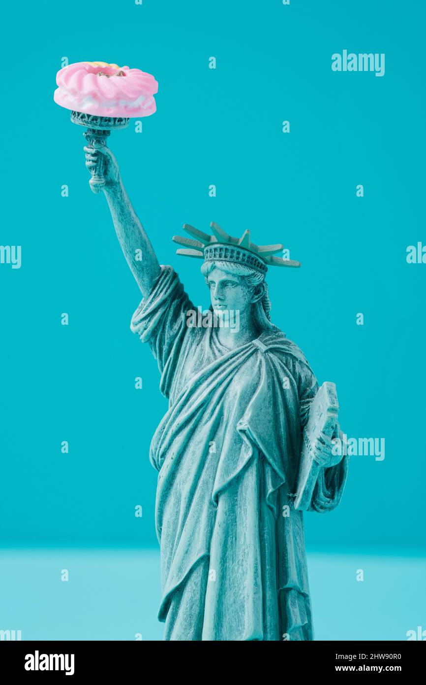 Statue of Liberty figurine with doughnut on the torch. USA politics conceptual background. Stock Photo
