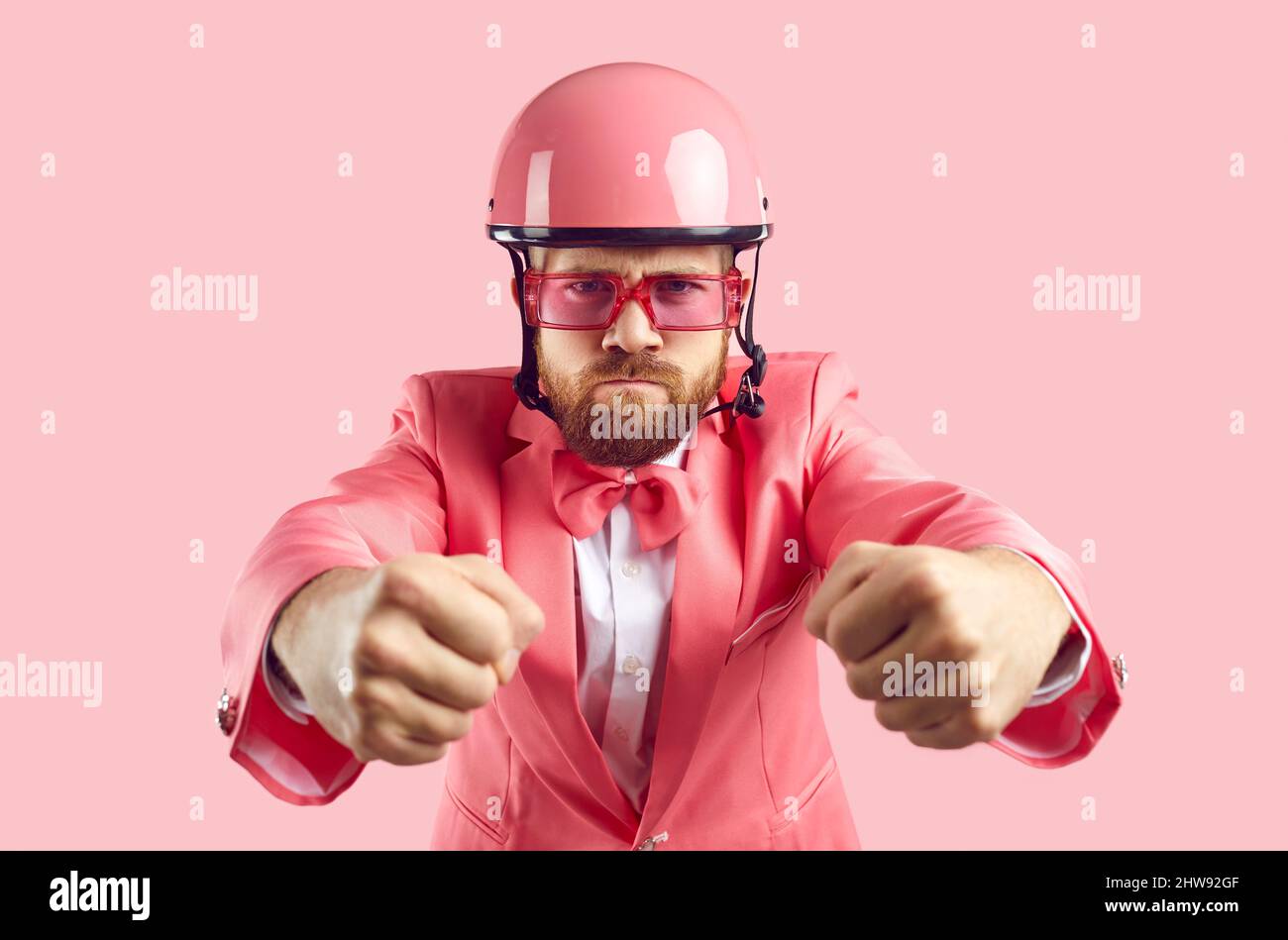 Funny man in pink suit and helmet driving invisible car with angry face expression Stock Photo