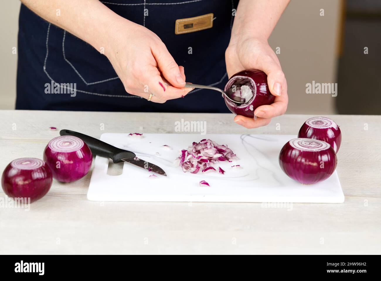 woman with spoon scoop out the inside of onion, leaving a layer of flesh around the perimeter. Onions stuffed with meat and vegetables recipe. Stock Photo