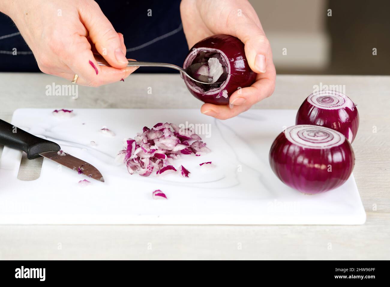 woman with spoon scoop out the inside of onion, leaving a layer of flesh around the perimeter. Onions stuffed with meat and vegetables recipe. Stock Photo