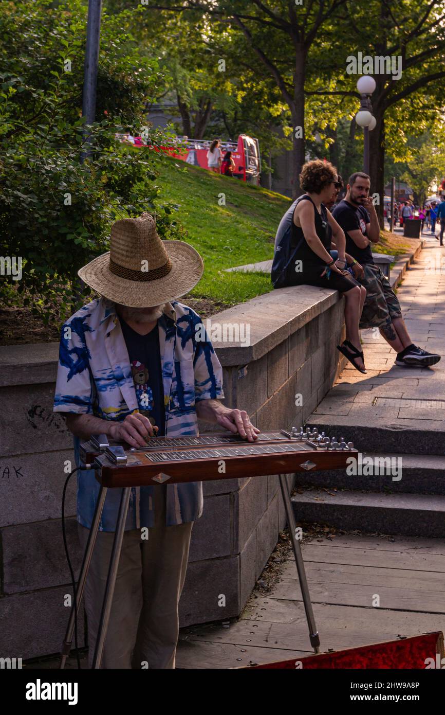 The Male entertainer musical artist playing music on an instrument slide guitar electric amplified on the street performer busking in public street Stock Photo