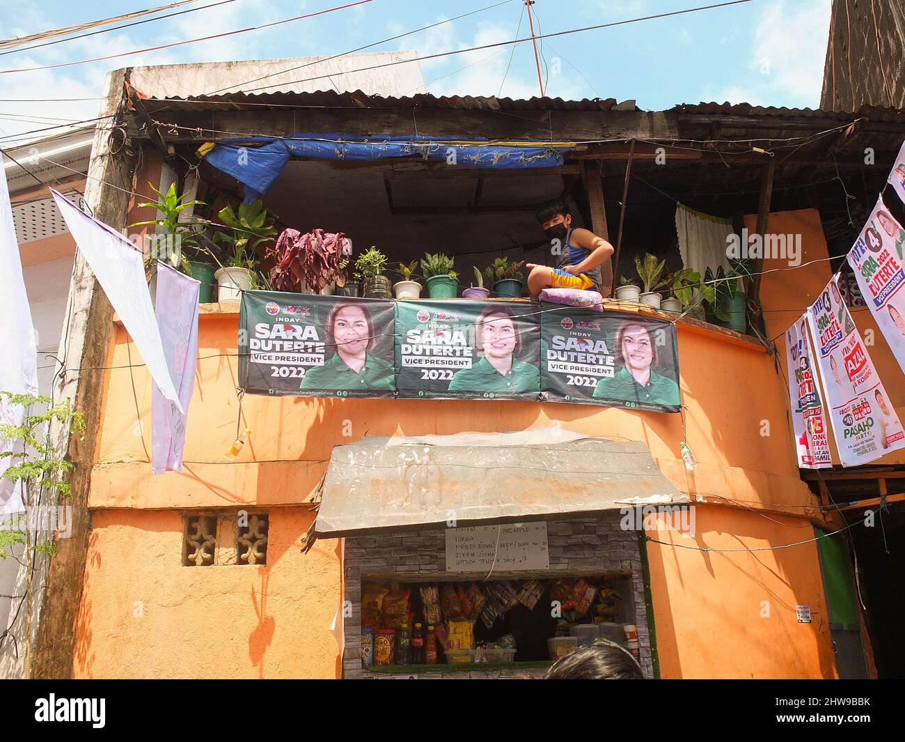 A young boy sits at the balcony of his house with large posters of Davao City Mayor Sara Duterte. Presidential daughter and Davao City Mayor Sara Duterte-Carpio visit Navotas City. It is the UniTeam's northern Metro Manila campaign swing. The Vice Presidential aspirant was also the chairperson of the Lakas-Christian Muslim Democrats (CMD) party. Her Presidential running mate Ferdinand 'Bongbong' Marcos Jr. was not present because of a campaign sortie in the province of Sorsogon. Stock Photo