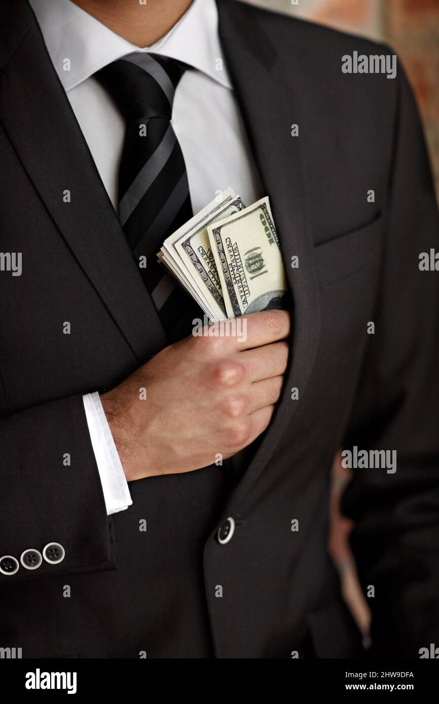 Hes not above accepting a bribe. Cropped shot of a man tucking a wad of cash into his jacket. Stock Photo