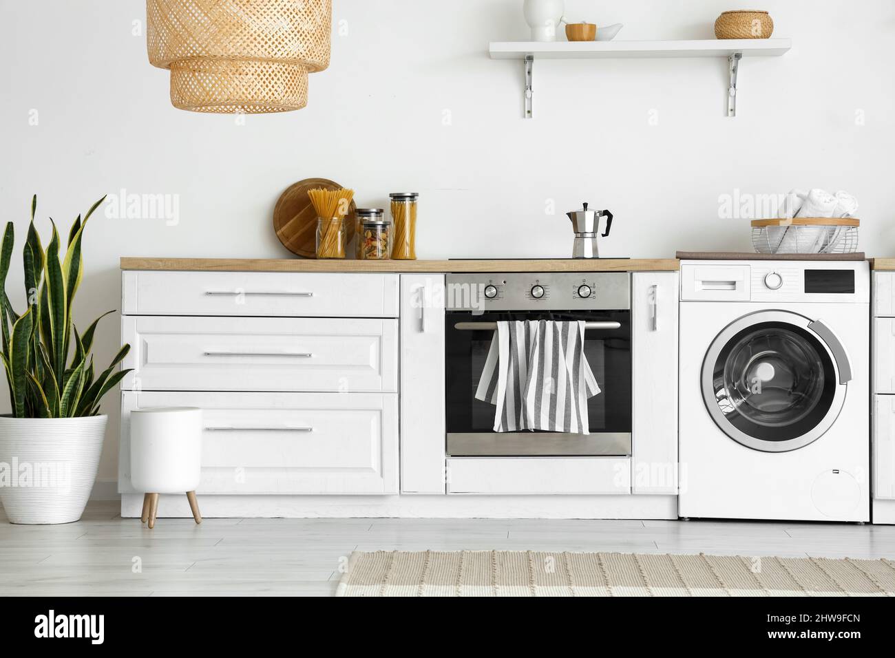 Interior of light kitchen with washing machine, oven and white counter