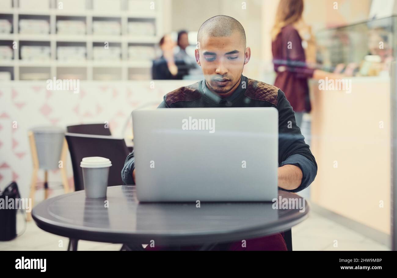 Enjoying some online time at his favourite cafe. Shot of a young man using his laptop in a coffee shop. Stock Photo