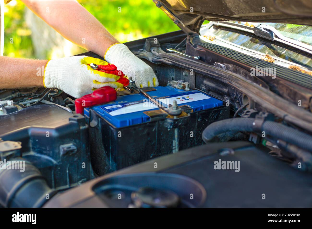Under the open hood of a car, an auto mechanic unscrews the car battery