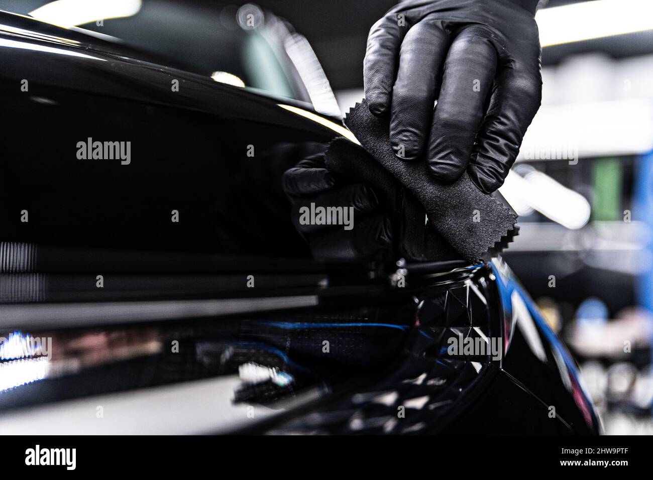 Car detailing studio specialist applying ceramic coating on black car. Stock Photo