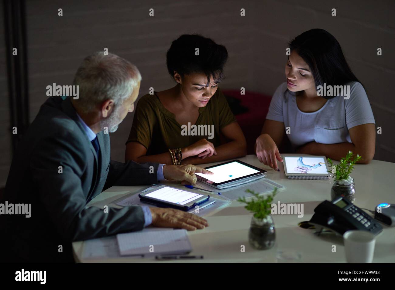 Combining their technical knowhow. Shot of a group colleagues using digital tablets while working late in an office. Stock Photo