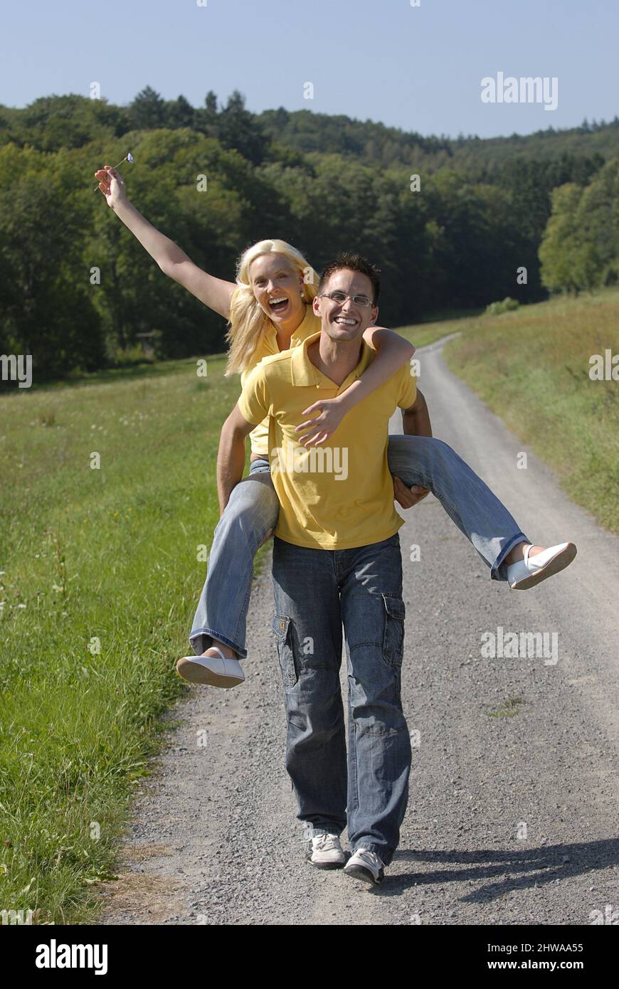 man walking along a country lane and carrying his wife piggyback, Germany Stock Photo