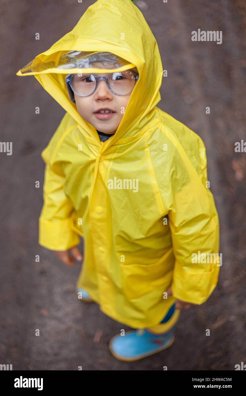 Child in a yellow raincoat walks in the forest and has fun Stock Photo
