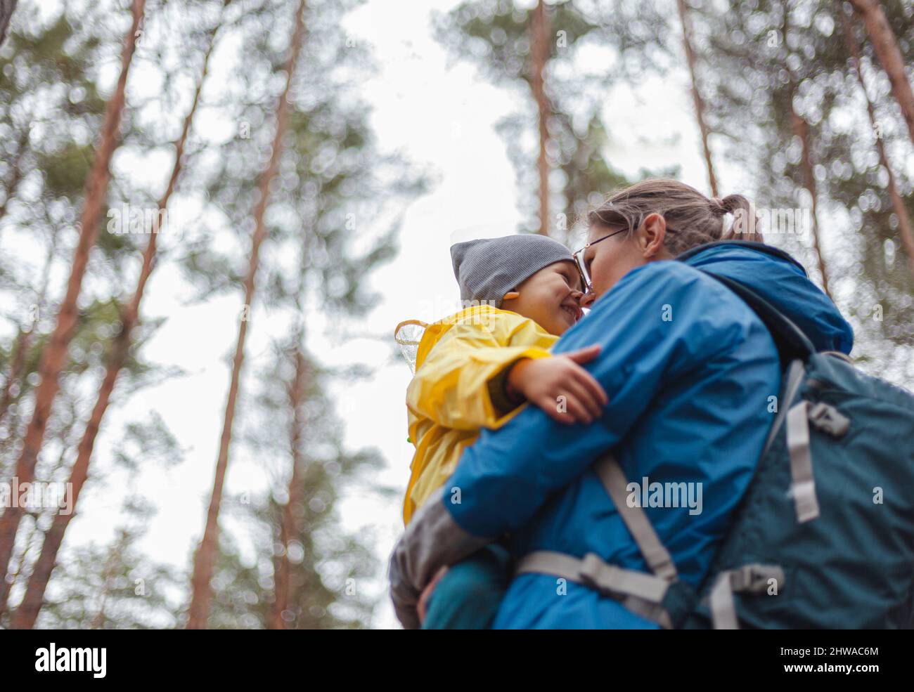 Happy family Mom and child walk in the forest after rain in raincoats together, hug and look at each other Stock Photo