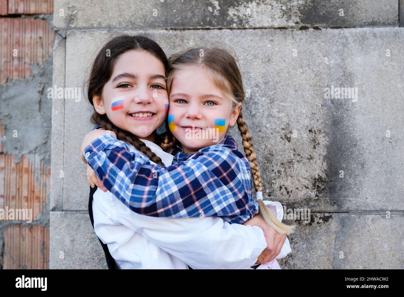 Portrait of two little girls embracing with Russian and Ukrainian flags on the faces. Concept of peace, stop the war and friendship of children Stock Photo
