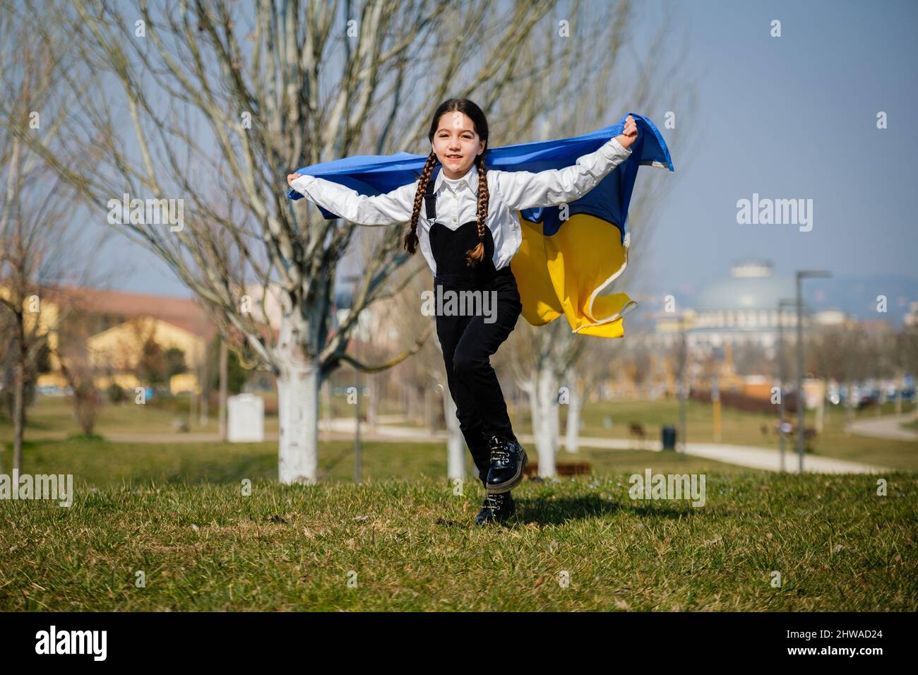 Happy Ukrainian girl running at the park waving the yellow and blue national flag. Concept of love for Ukraine. Independence, flag, Constitution Day Stock Photo