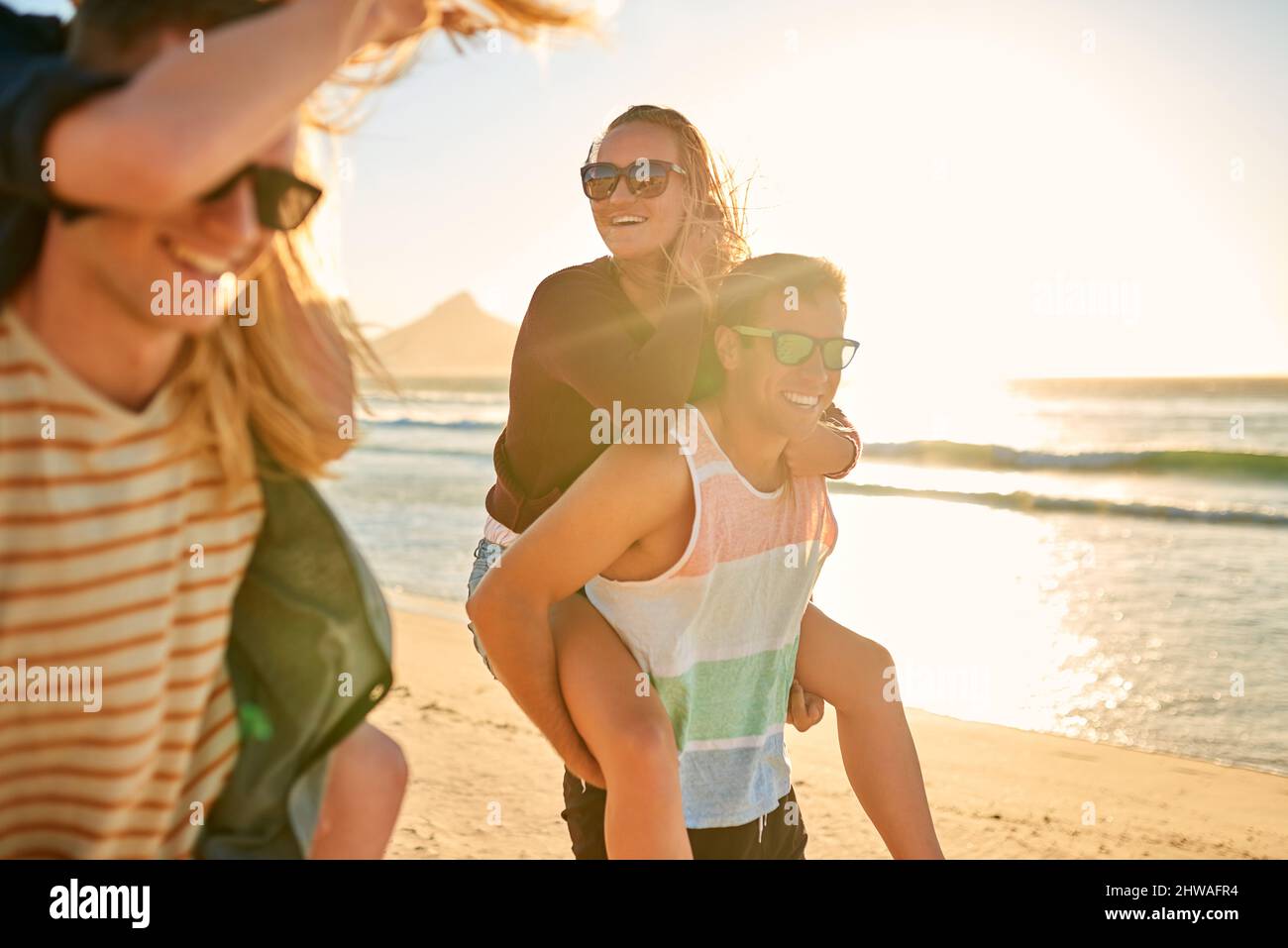 Love, friends and laughter. Cropped shot of two affectionate young men piggybacking their girlfriends at the beach. Stock Photo