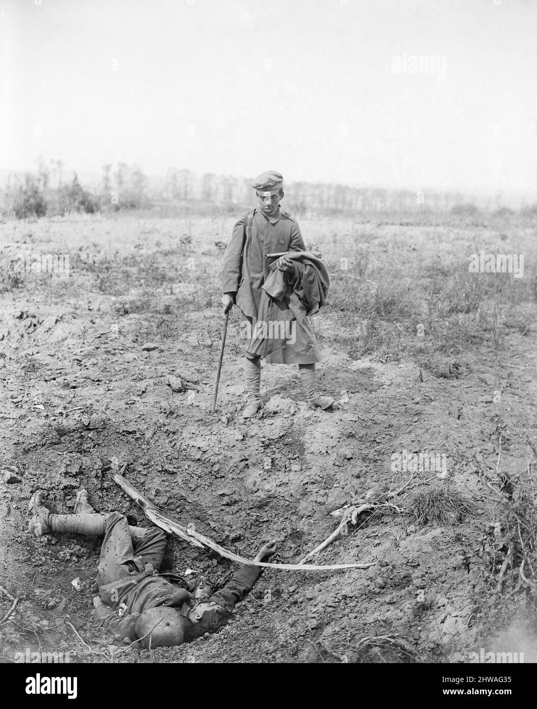 Capture of Meteren by the 9th (Scottish) Division, 19th July 1918. A captured German prisoner, carrying a Very Light Pistol (flare gun), on his way back (unescorted) looking at a dead comrade lying at the bottom of a shell-hole, 20th July 1918. Stock Photo