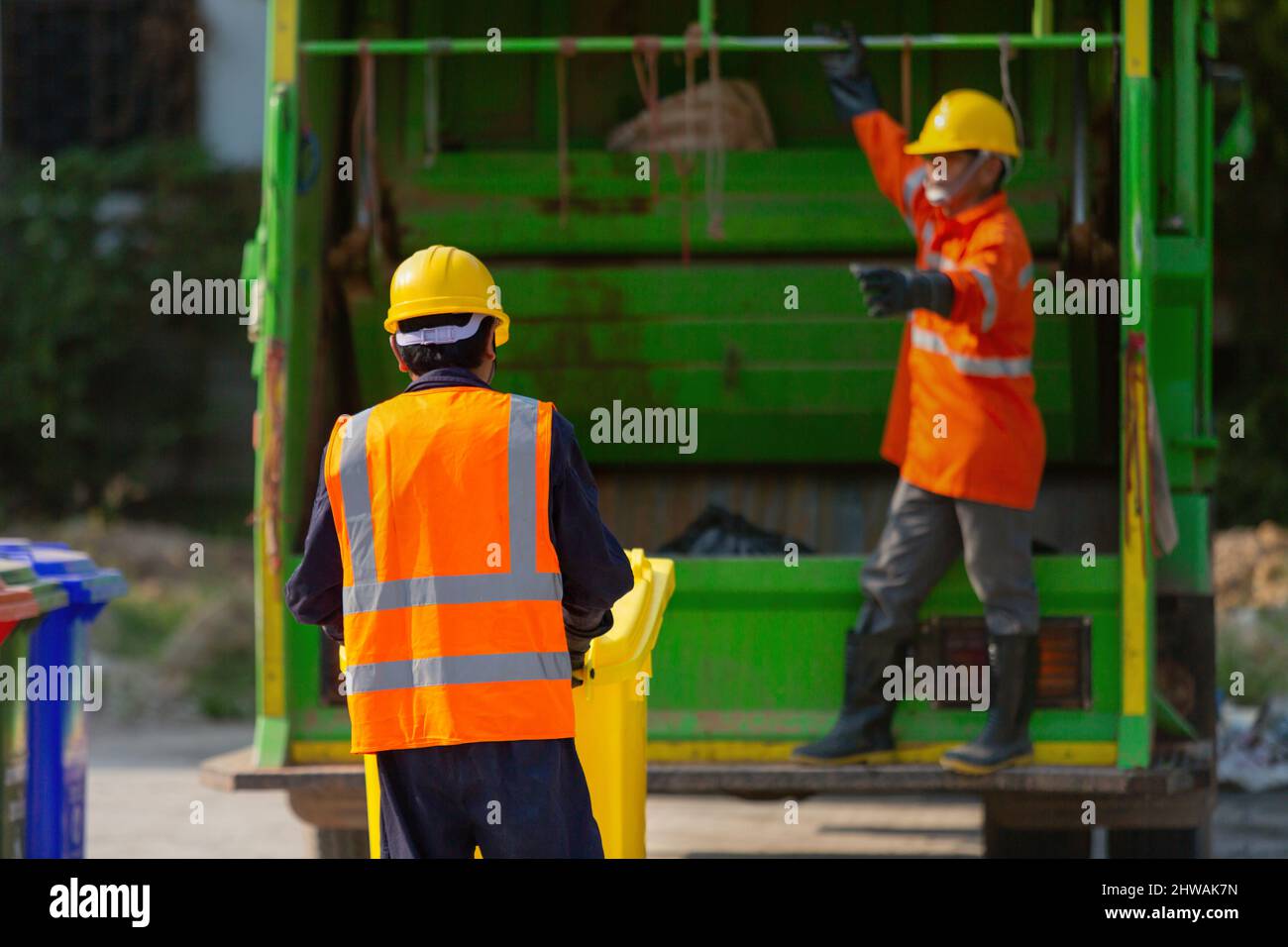 Garbage collector, teamwork garbage men working together on emptying dustbins for trash removal with truck loading waste and trash bin. Stock Photo