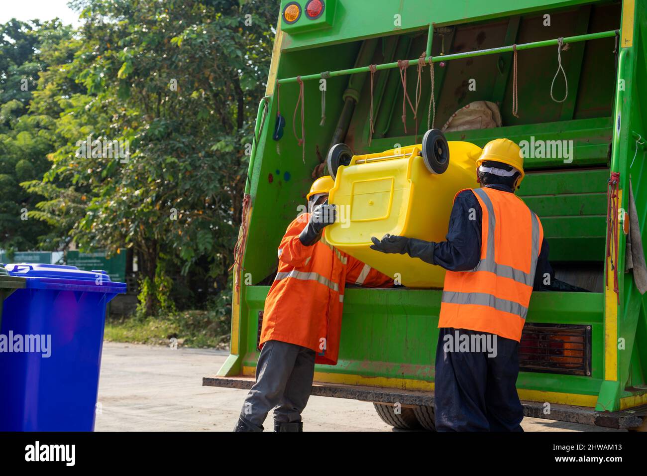 Garbage collector, Two garbage men working together on emptying dustbins for trash removal with truck loading waste and trash bin. Stock Photo