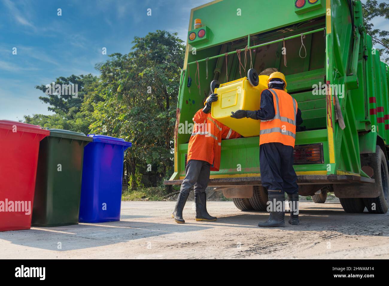 Teamwork garbage men working together on emptying dustbins for trash removal with truck loading waste and trash bin. Garbage collector. Stock Photo