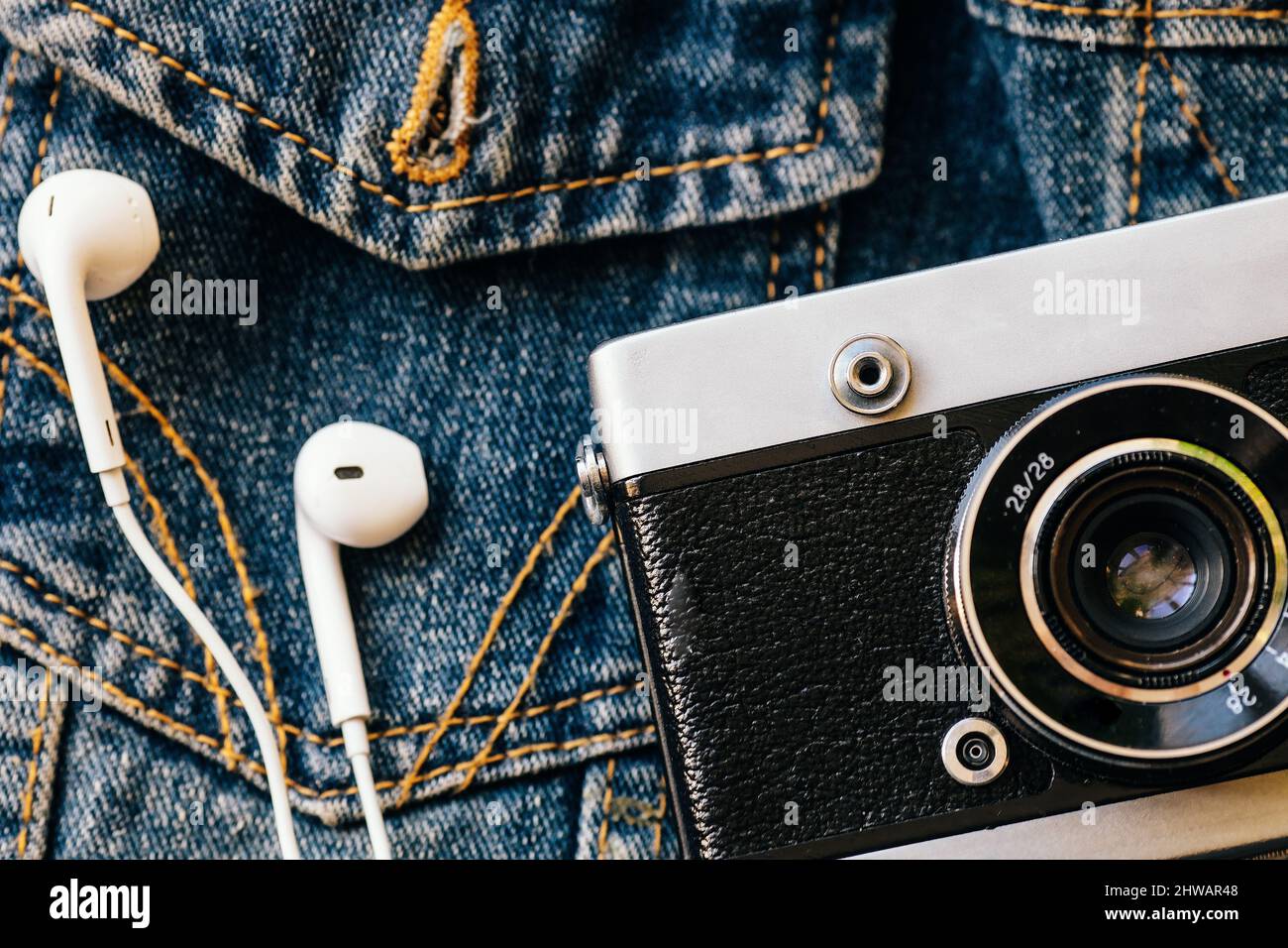 Film camera and white wired headphones lie against background of denim. Fashionable hipster background. Retro style. Photographer's Day. Top view Stock Photo