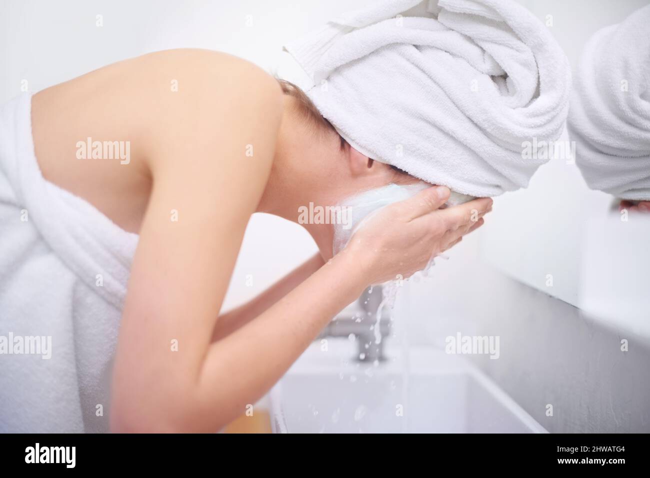 Final stages of her beauty treatment. A young woman washing off her facial mask in her bathroom. Stock Photo