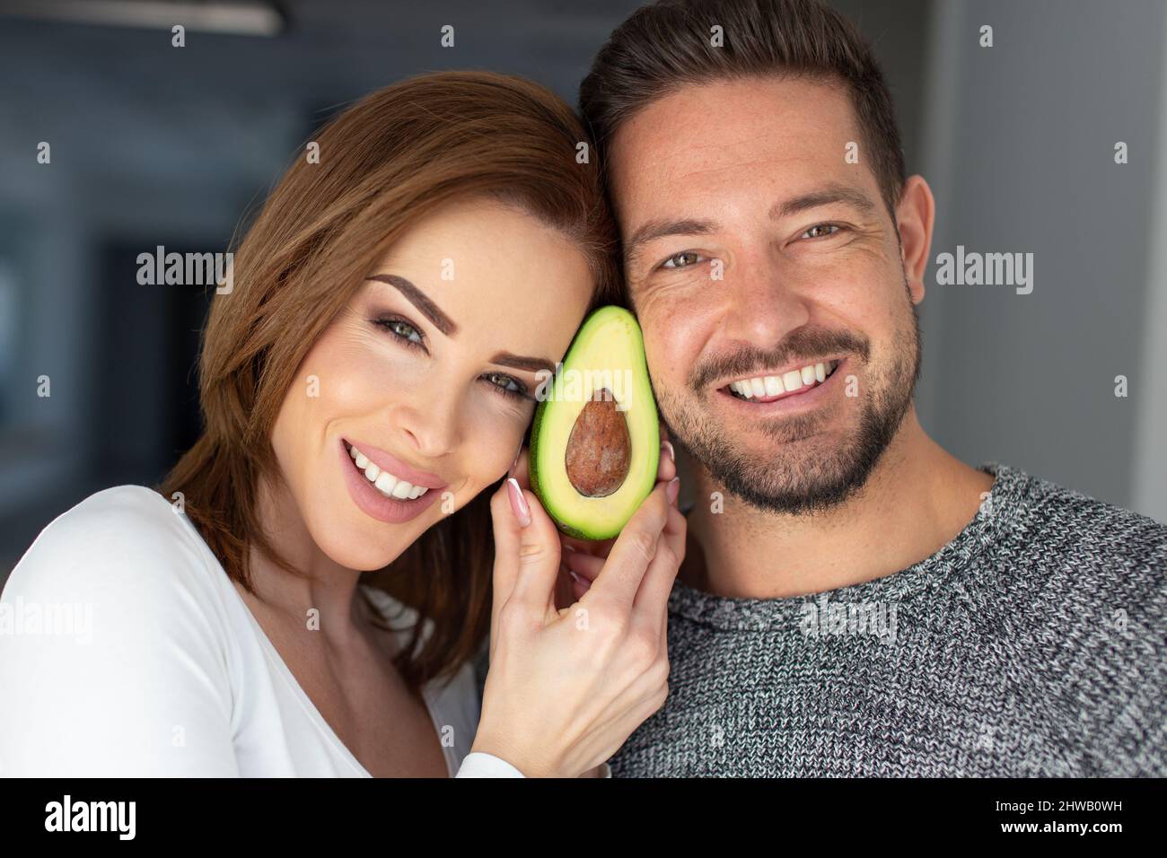Happy young Caucasian couple holding avocado at face portrait Stock Photo