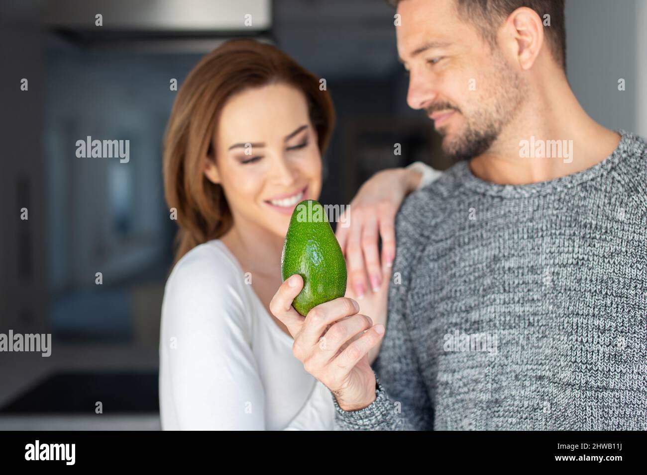 Young Caucasian man offering avocado to woman indoors, depth of field Stock Photo